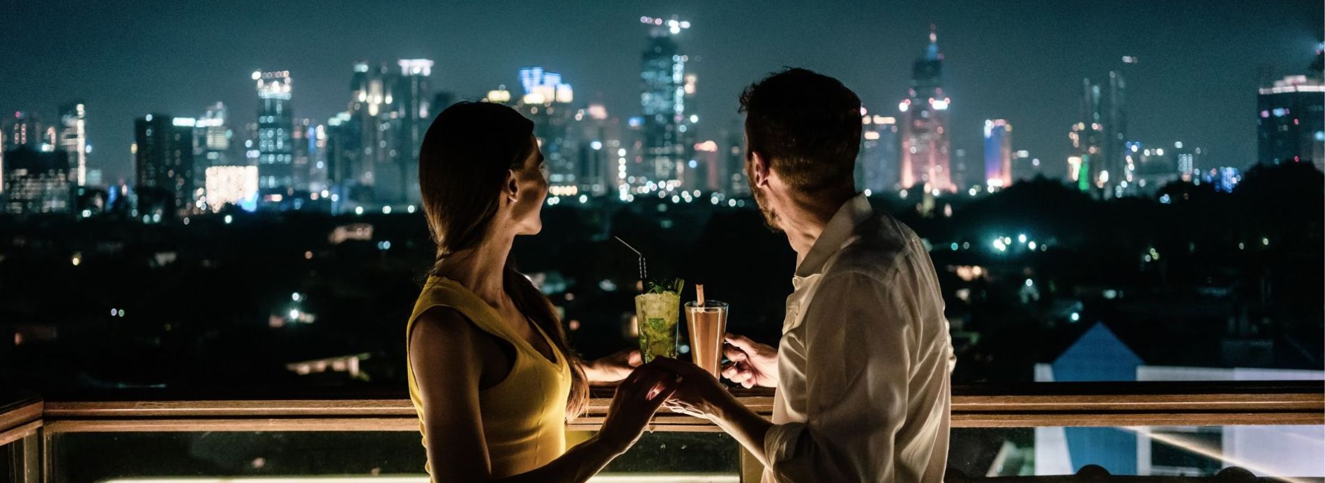 Couple having cocktails at rooftop bar overlooking a city skyline